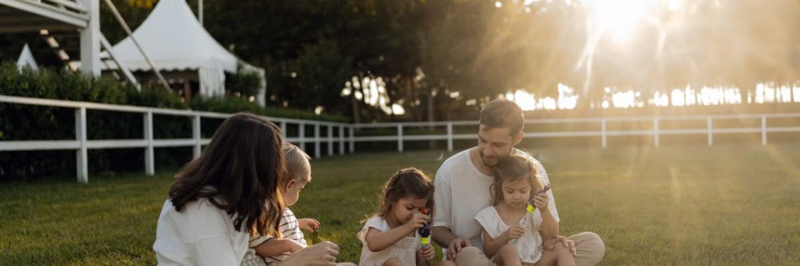 Family sitting on grass enjoying leisure time outdoors, with sun setting in the background.