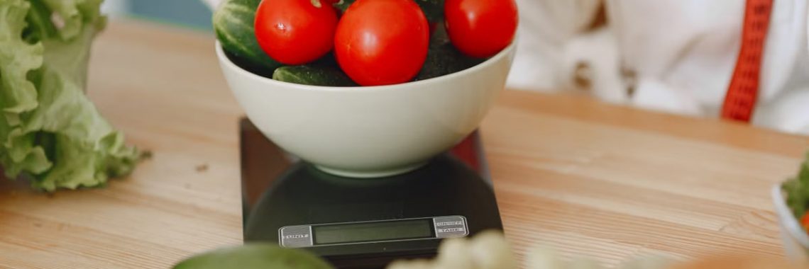 Colorful fresh vegetables including tomatoes and cucumbers on a kitchen scale for healthy eating.